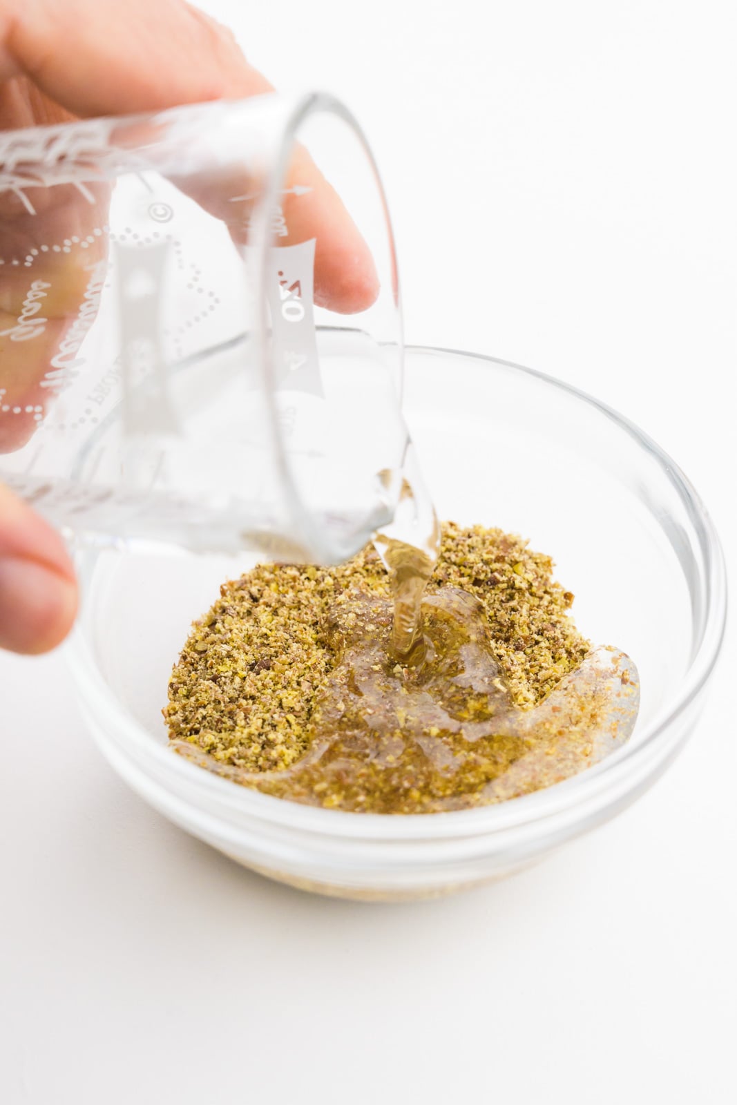A hand holds a glass of water and is pouring it into a bowl with ground flax seeds.