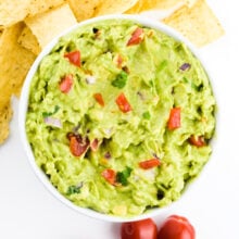 Looking down on a bowl of guacamole with tortilla chips and cherry tomatoes around it.