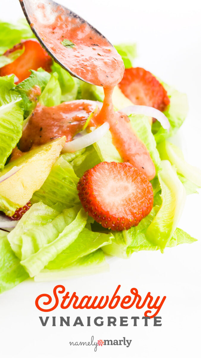 Spoon drizzling strawberry vinaigrette over a fresh salad with lettuce and sliced strawberries.