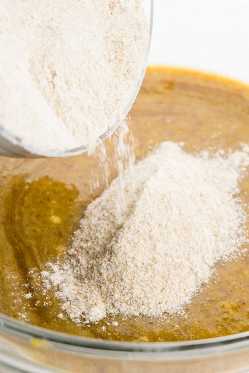 A bowl of flour is being poured into batter.