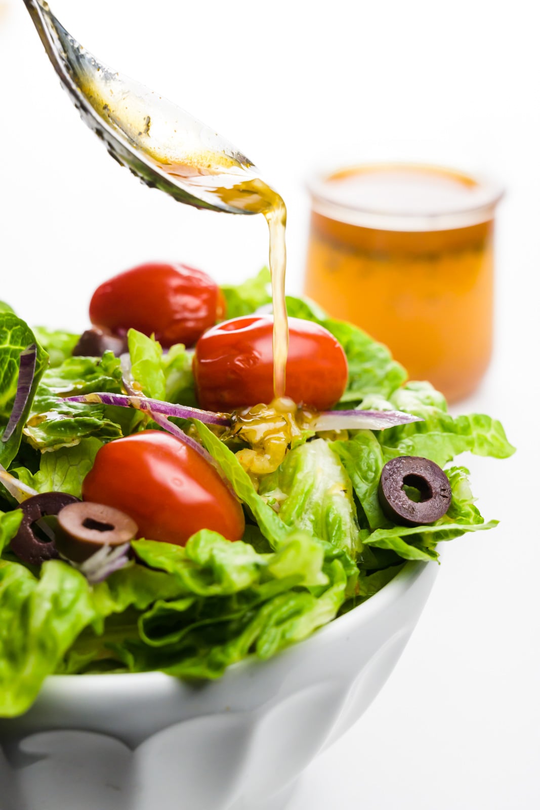 A spoon pours dressing over a salad. A jar with more dressing sits behind it.