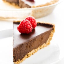 A slice of chocolate pie has raspberries on top. The rest of the pie is behind it.