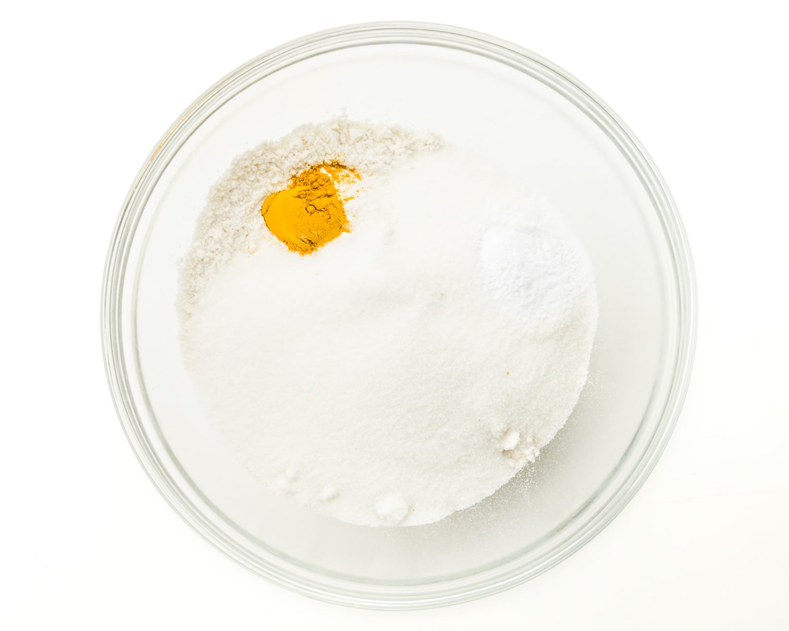 Looking down on a mixing bowl with flour and other ingredients, including turmeric.