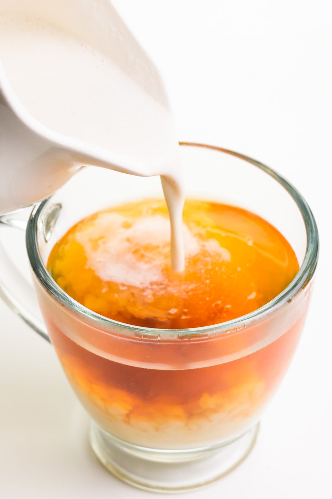 Milk is being poured into a hot cup of black tea.