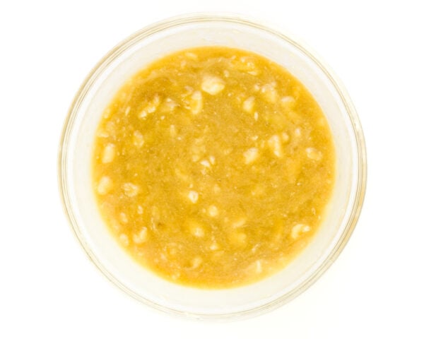 A mixture of mashed bananas and other ingredients are in the bottom of a glass bowl.