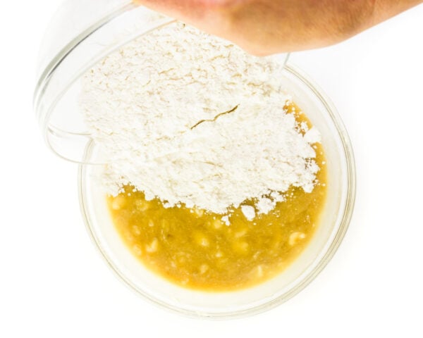 Gluten-free flour is being poured into a bowl with the wet ingredients.