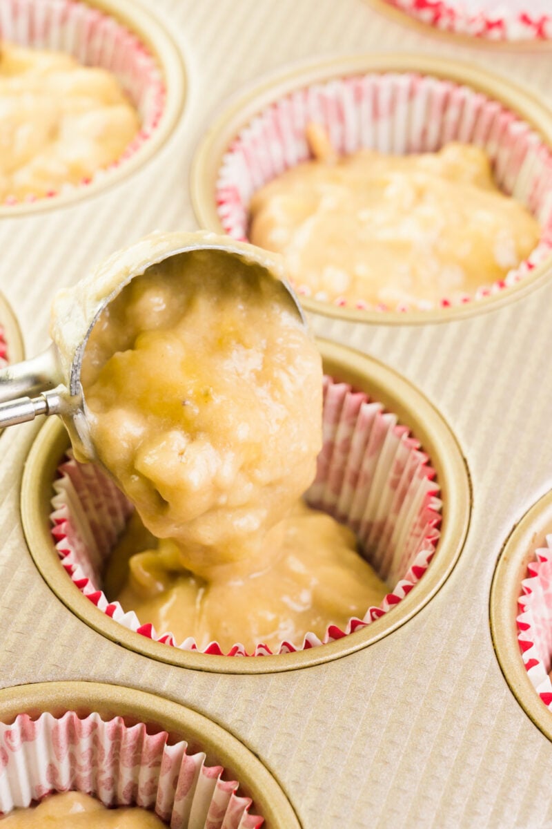 Batter is being poured into a muffin compartment lined with papers.