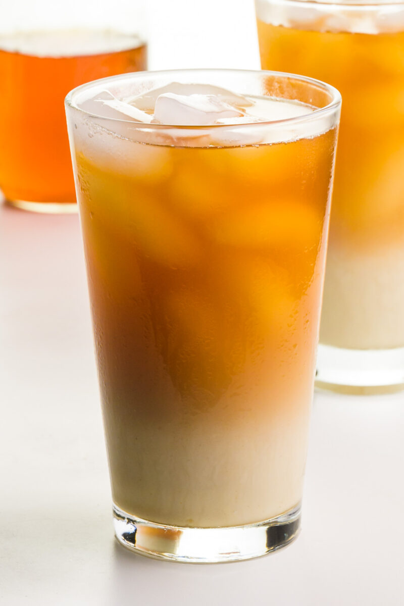 Homemade Iced Chai Latte A glass of chai tea latte with another glass behind it and chai tea concentrate.