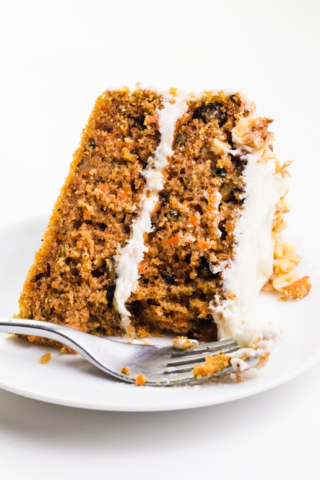 A slice of carrot cake sits on its side on a plate with a fork in front of it.