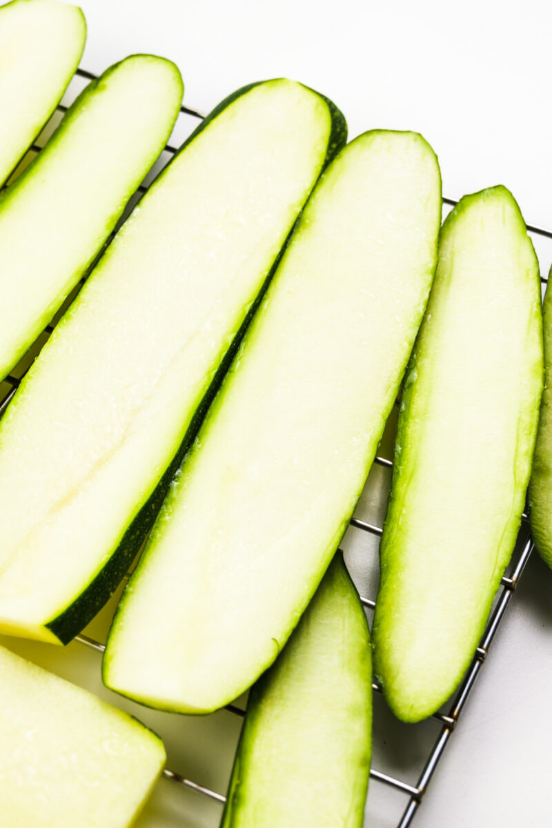 Zucchini slices are sitting on a wire rack.