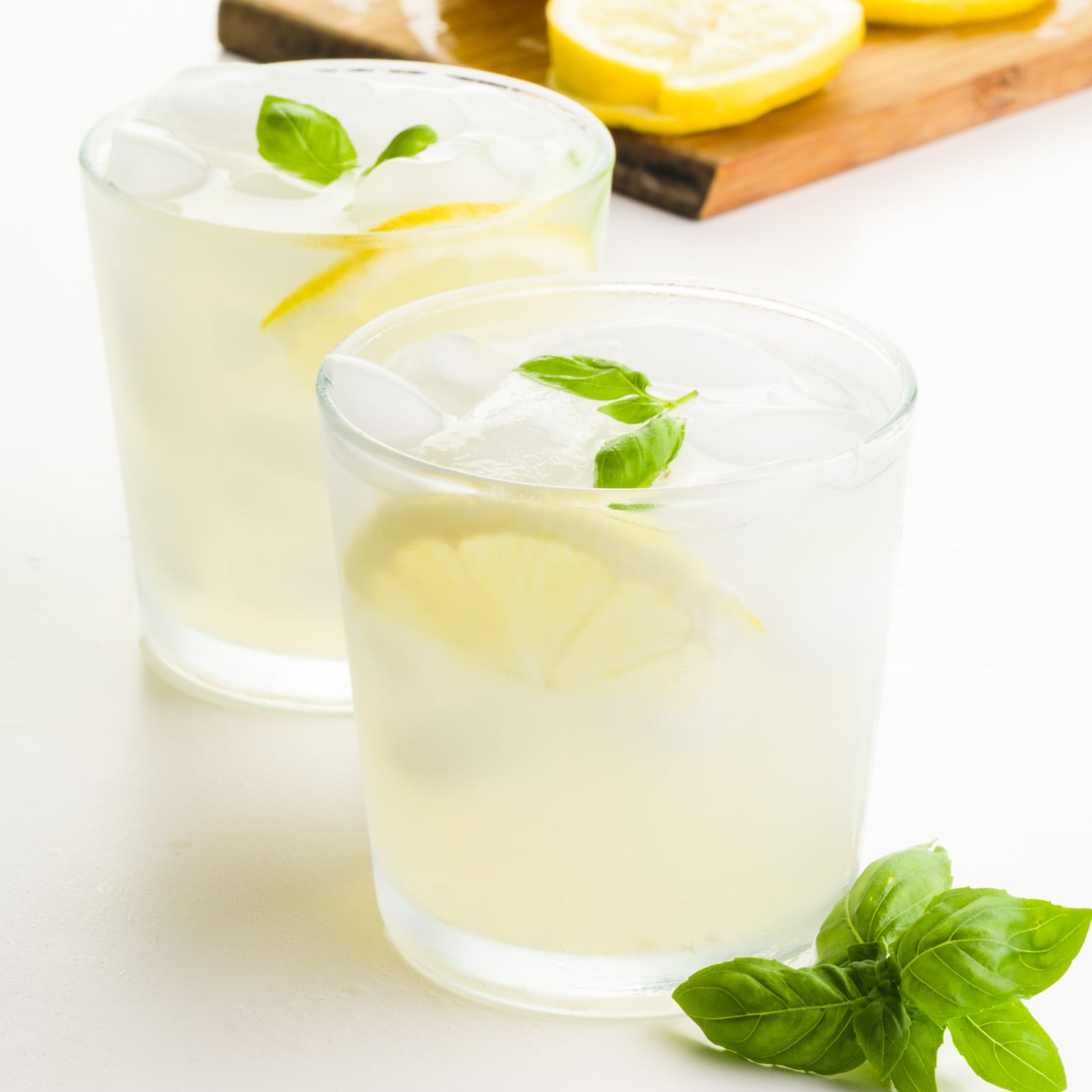 Two glasses hold lemonade with lemon slices and fresh basil sprigs.