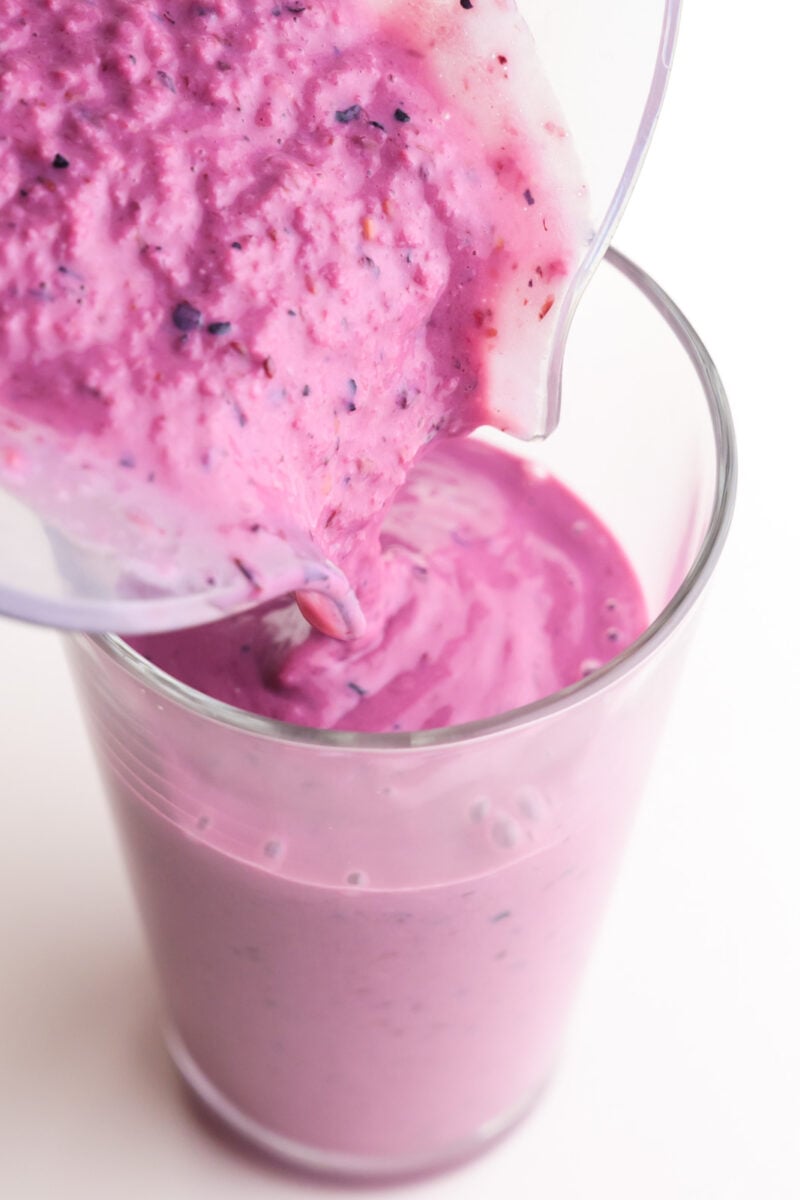 A pink smoothie is being poured into a glass.