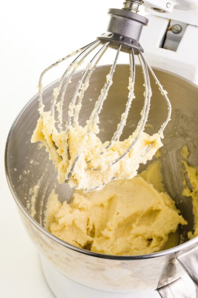 Vegan butter has been combined in a mixing bowl with sugar. The prongs of the mixer are coated with the mixture too.