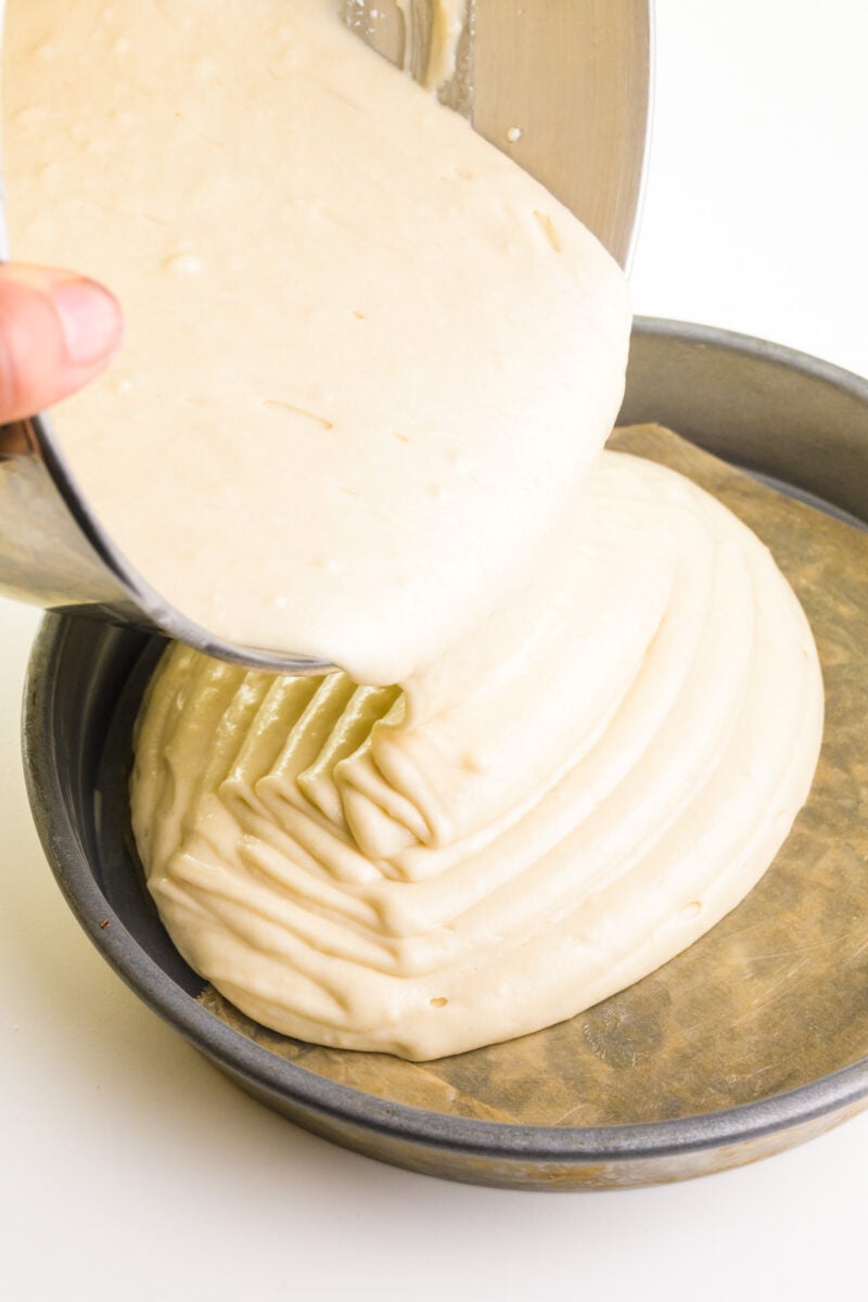 Cake batter is being poured into a round cake pan.