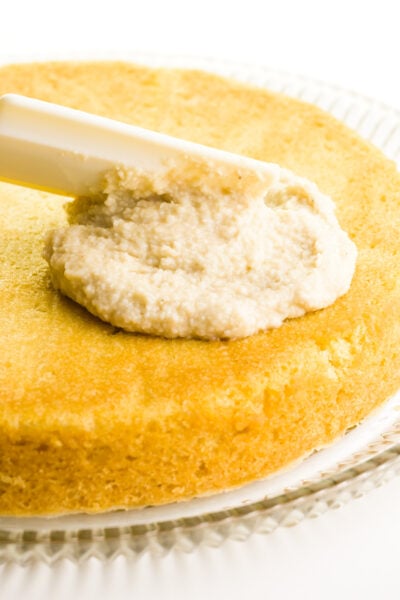 A creamy filling is being spread on top of a round cake layer.