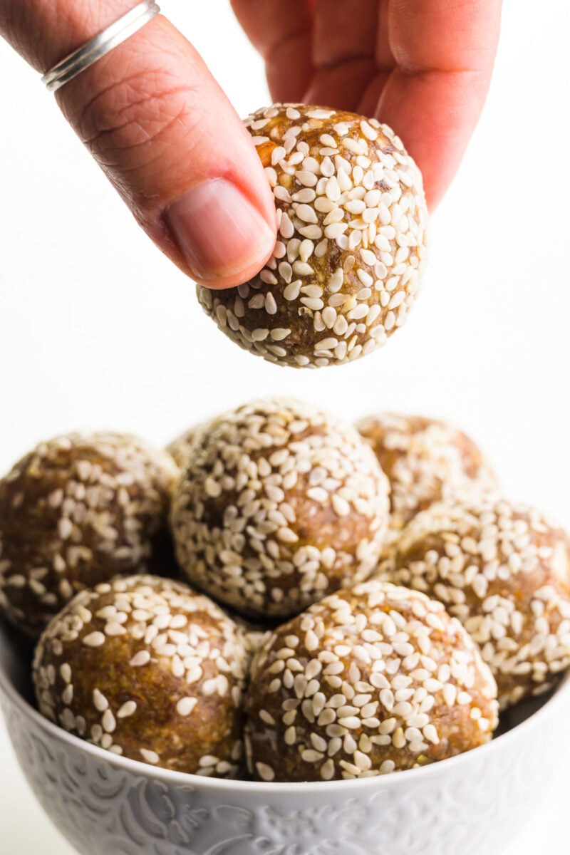 A hand holds a date ball above a bowl full of more of the treats.