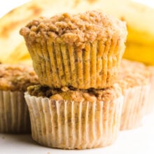 Two muffins are stacked on top of each other with more muffins and bananas behind them.