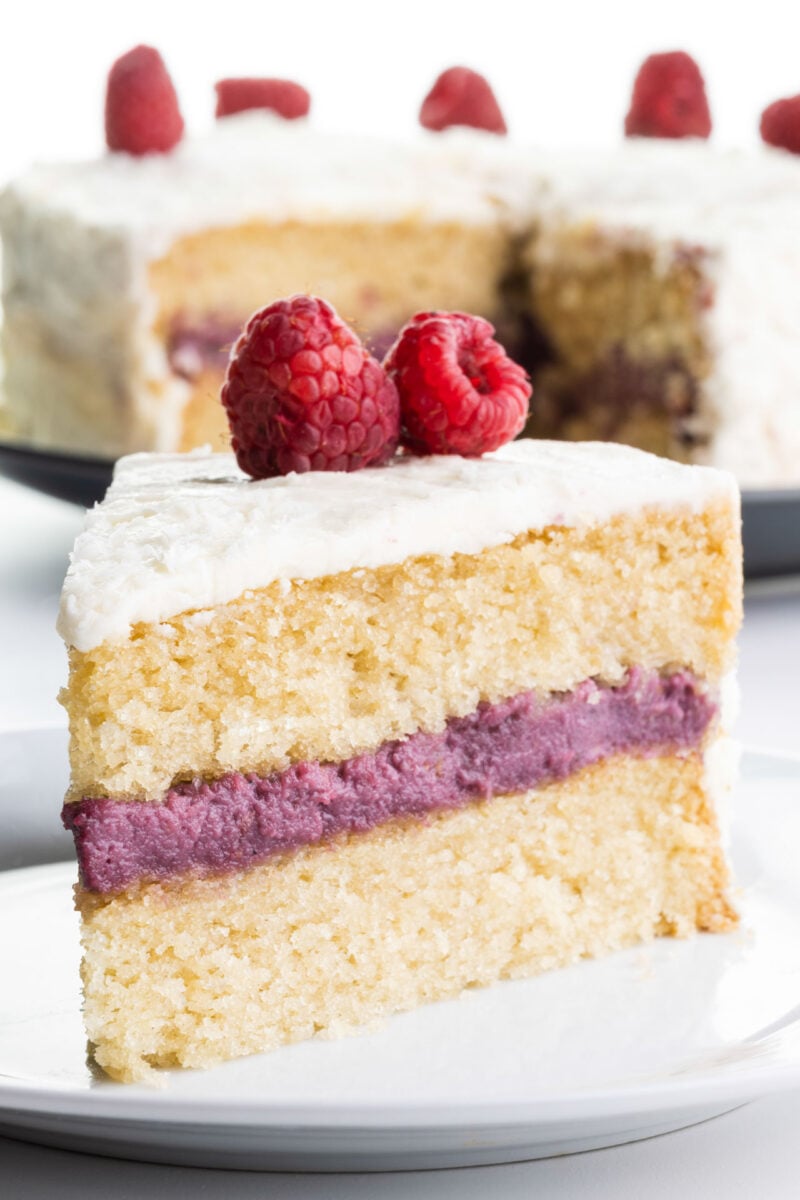 A slice of raspberry coconut cake on a plate sits in front of the rest of the cake.