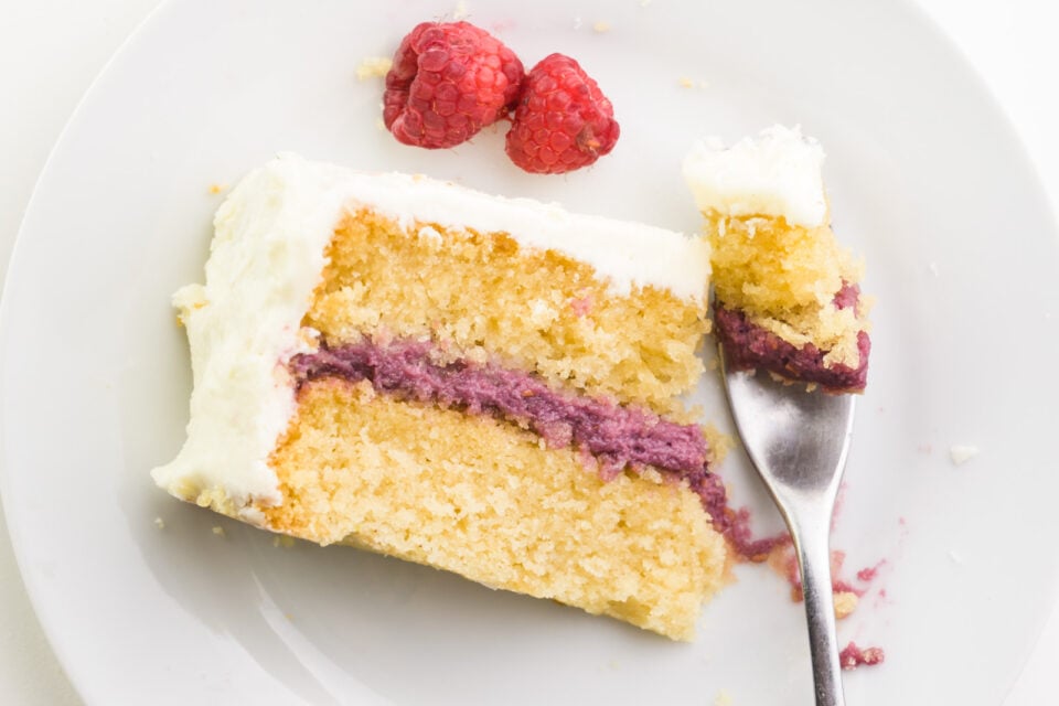 Looking down on a slice of cake on a plate. A fork has taken a bite out and is sitting next to the cake.