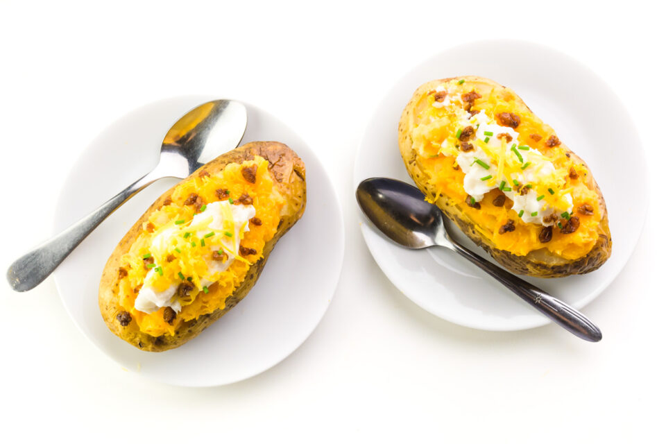 Looking down on two plates, both with cheesy bake potatoes with spoons sitting next to them.