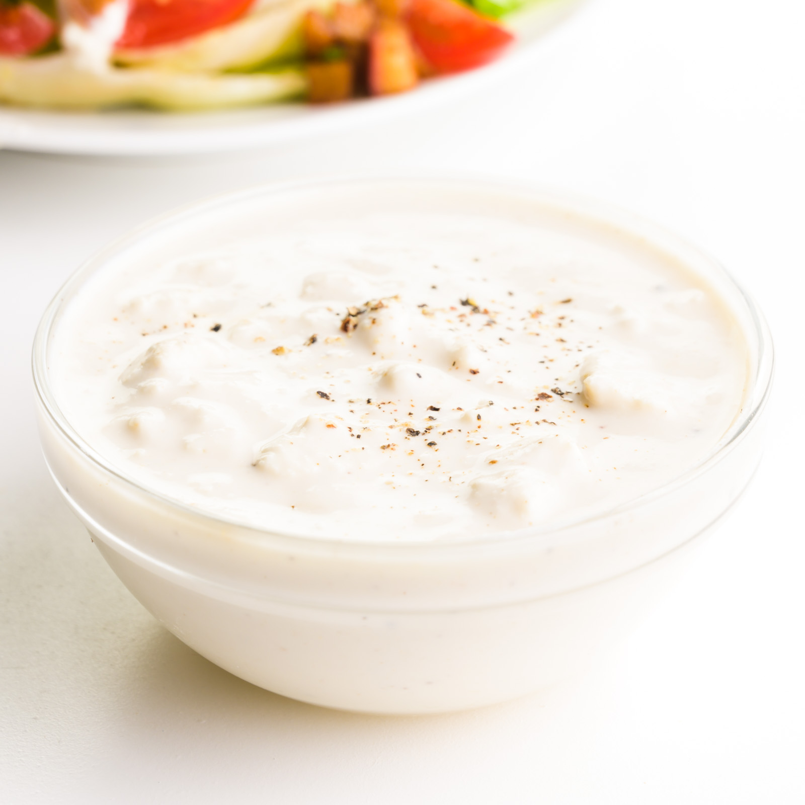 A bowl of vegan blue cheese dressing sits in front of a salad.