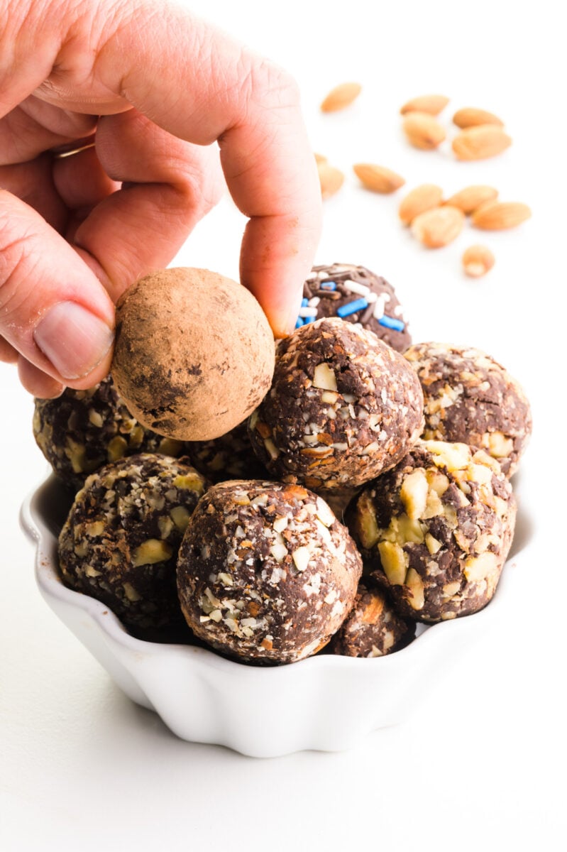 A hand grabs a chocolate truffle from a bowl full of them.