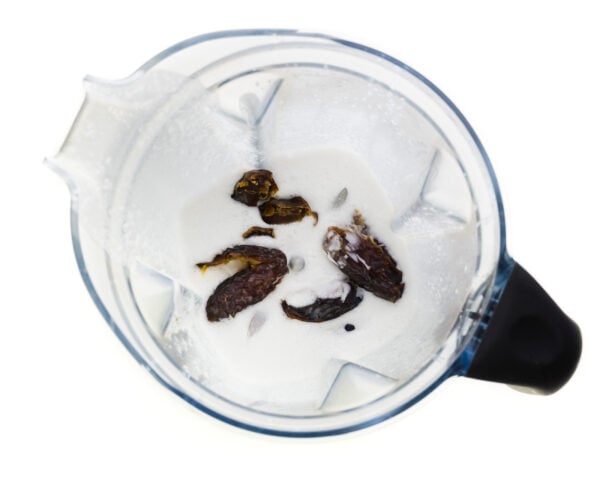 Looking down on a blender jar with coconut milk and dates in the bottom.