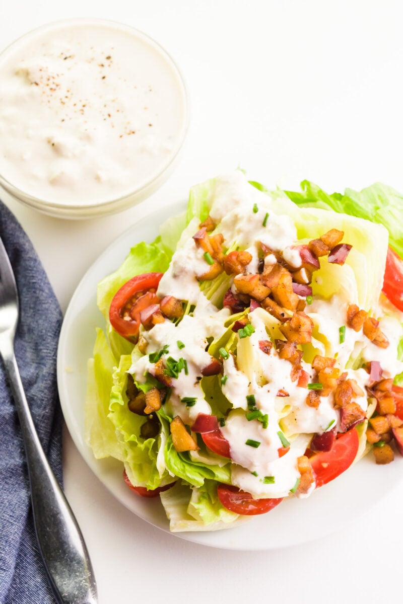 Looking down on a salad with vegan blue cheese dressing drizzled over the top and a bowl of the dressing sitting beside it.