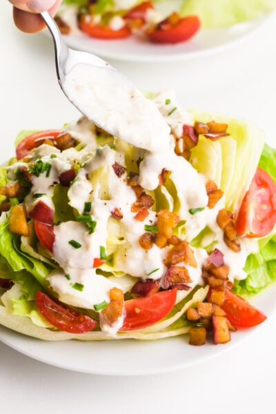 A spoon drizzles dressing over a plate of greens and veggies.