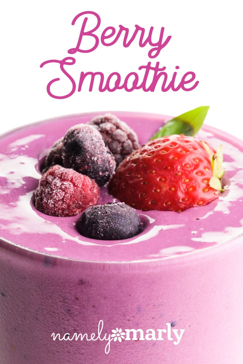 Berry smoothie topped with strawberries and various frozen berries, in a light pink cup.