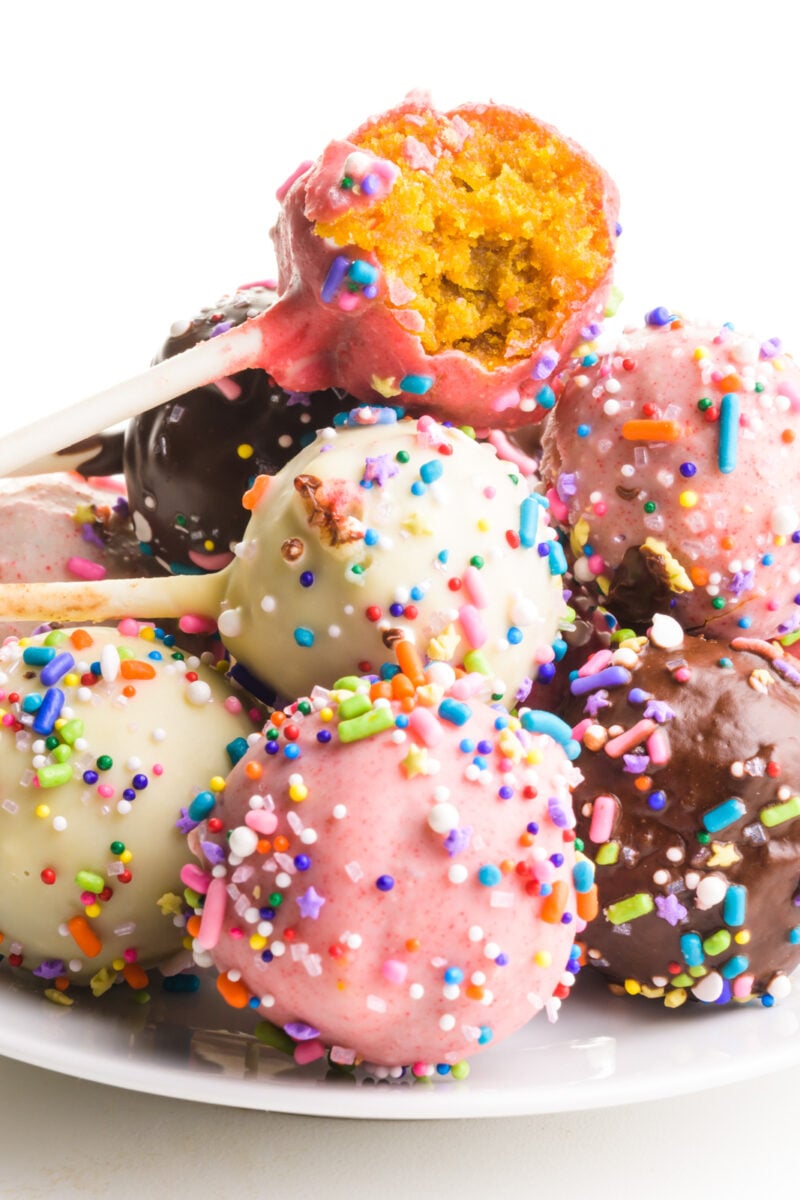Several vegan cake pops sit on a plate. The top one has a bite taken out.