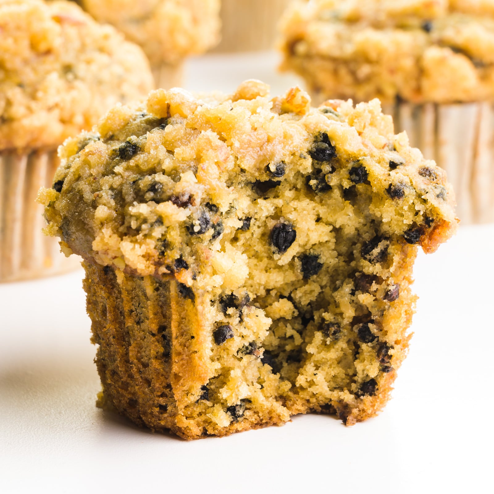 An elderberry muffin has a bite taken out, showing lots of berries. There are more muffins behind it.