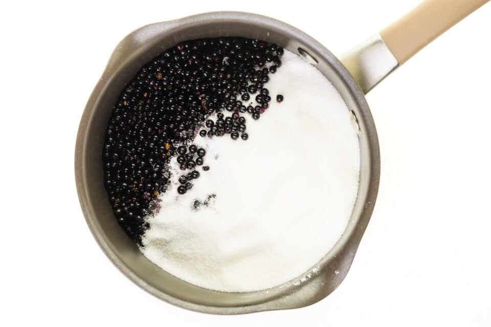 Looking down on a saucepan full of elderberries and sugar.