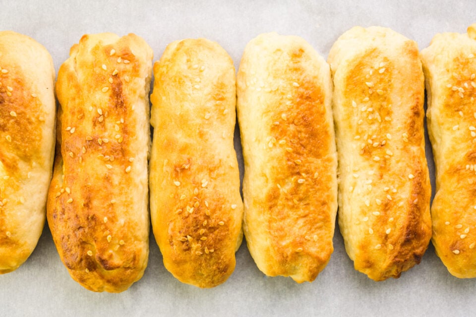 Baked buns sit in a row on a baking sheet lined with parchment paper.