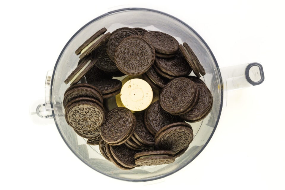 Several chocolate sandwich cookies are in the bottom of a food processor bowl.