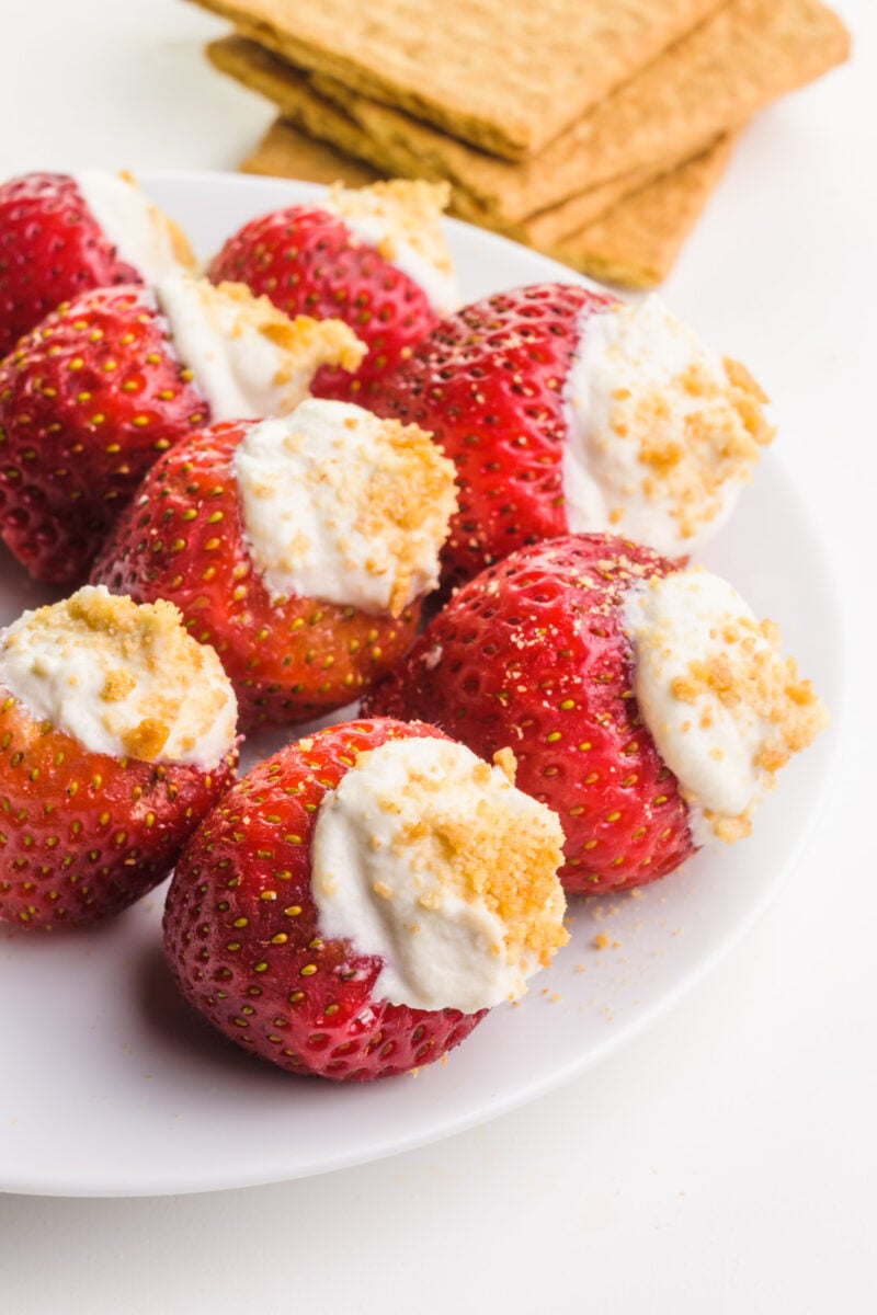 Several stuffed strawberries sit on a plate. There's a stack of graham crackers in the background.