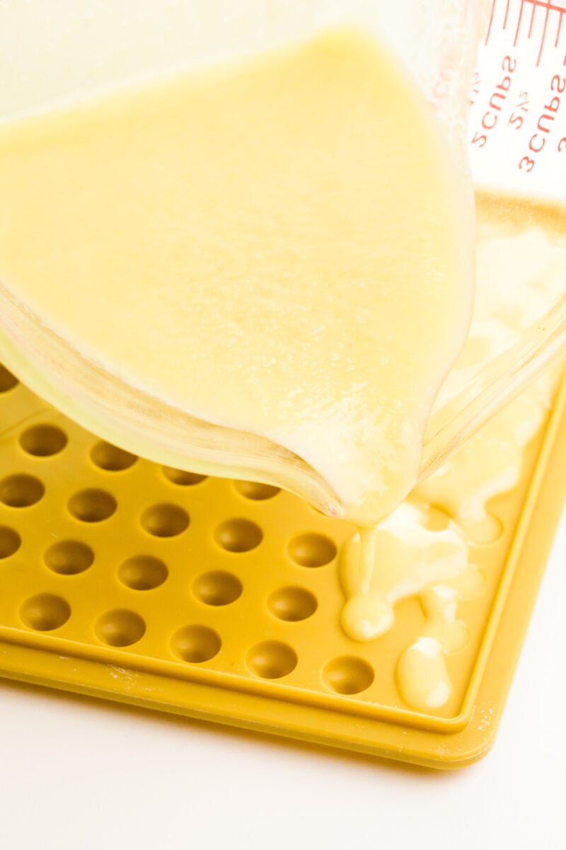 A pyrex measuring cup is full of melted white chocolate, pouring it into a mold to make chocolate chips.