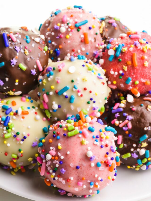 Several cake balls are on a plate. They're all different colors with multi-colored sprinkles.