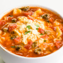 A bowl of tomato-based soup shows noodles and a creamy sauce on top.