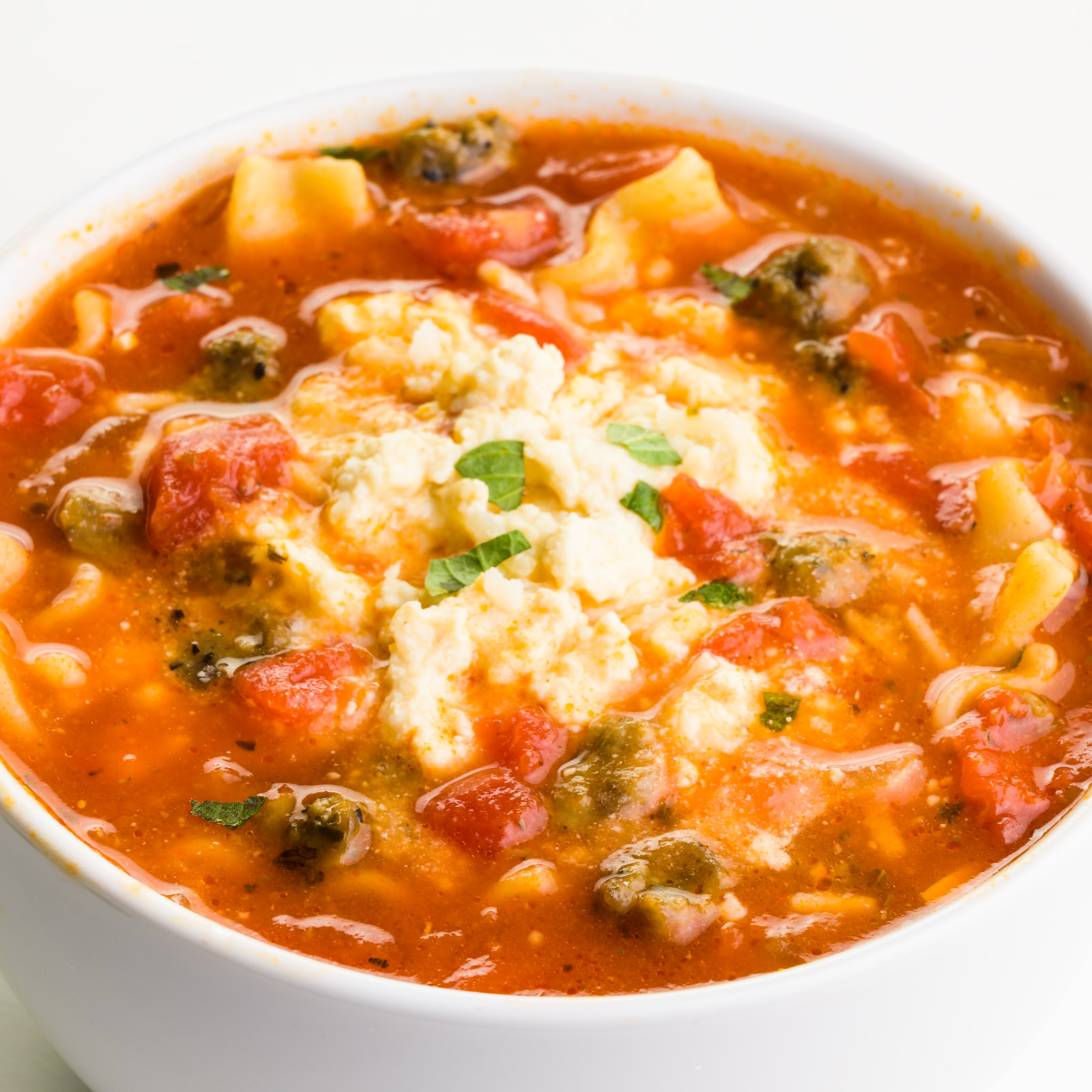 A bowl of tomato-based soup shows noodles and a creamy sauce on top.