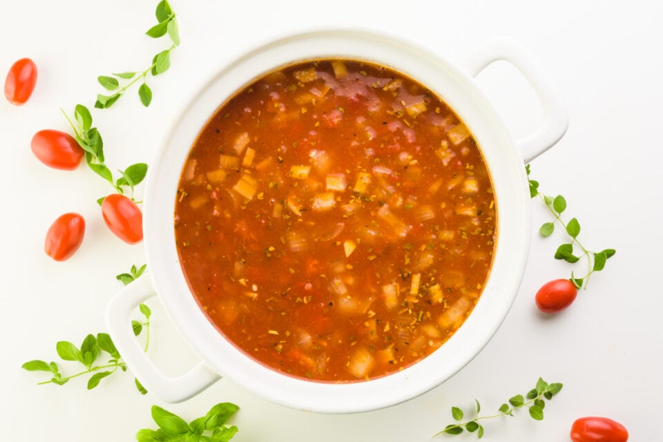 Looking down on a pot full of soup. There are cherry tomatoes and fresh herbs around it.