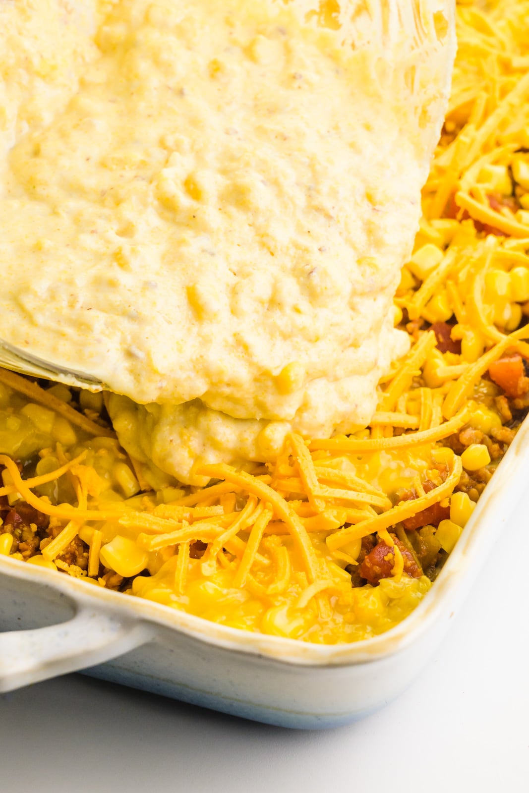 A cornbread batter is being poured over a casserole dish.