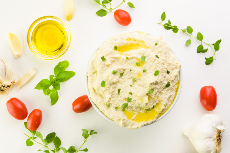 Looking down on a bowl of vegan ricotta cheese sitting next to tomatoes, herbs, garlic cloves, and a small bowl of olive oil.