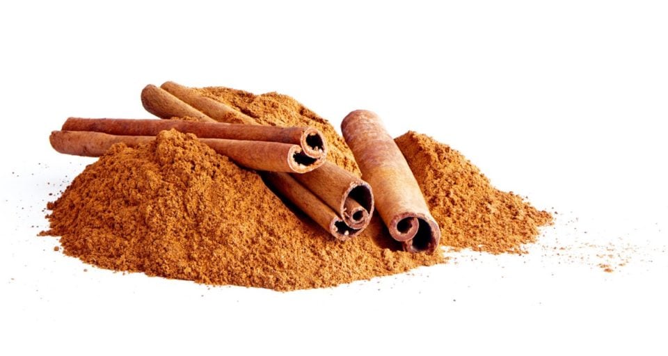 A pile of ground cinnamon with several cinnamon sticks on top.