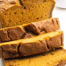 A loaf of vegan pumpkin bread has several slices cut. There's a bowl of Pumpkin Puree next to the loaf.