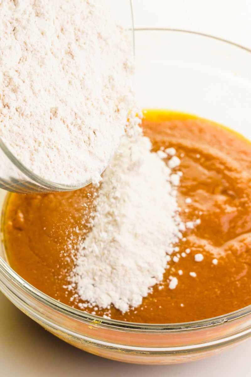 Flour is being poured into a pumpkin batter mixture.