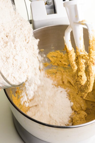 Flour is being poured into a mixing bowl with cookie batter.