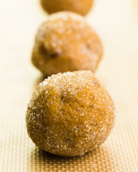 Cookie dough balls are coated in sugar and sitting on a baking sheet, ready to go into the oven.