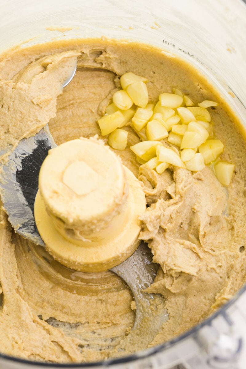 Looking down on a food processor full of tahini paste and cooked garlic.