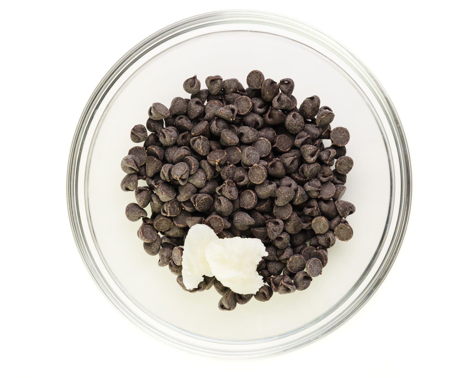 Chocolate chips are in a glass bowl along with with some coconut oil.